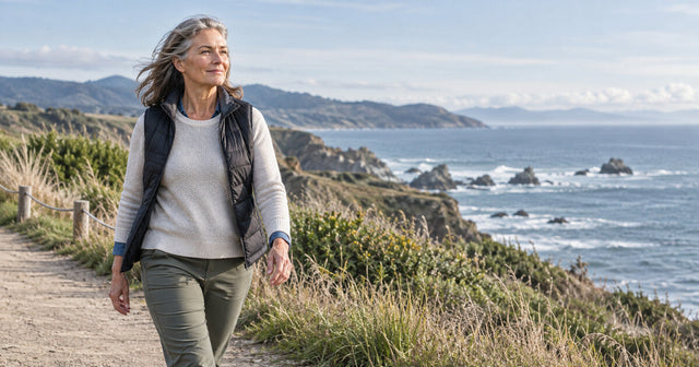 Mature woman walking along a coastal trail, representing an active, healthy lifestyle and well-being during menopause.